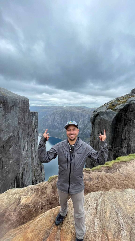 Jason Moore standing near a cliff in Norway with his arms raised