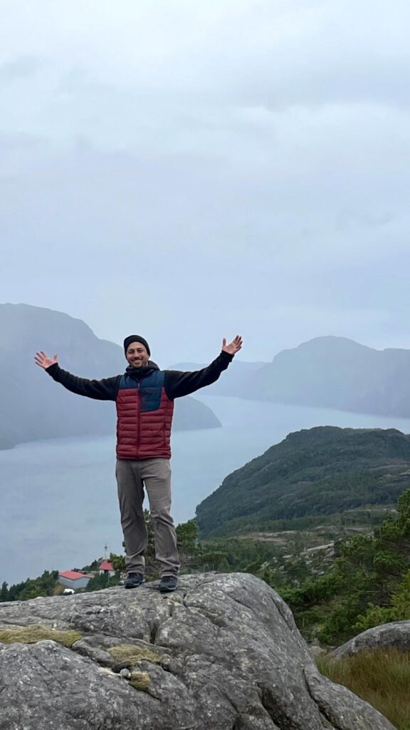 Jason Moore standing on a cliff in Norway with his arms raised