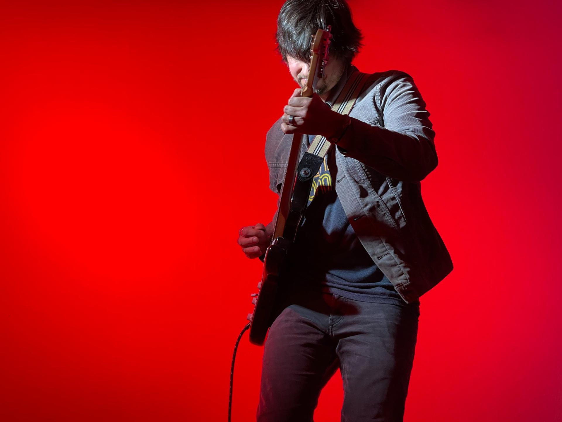 Jason Moore playing guitar on red background